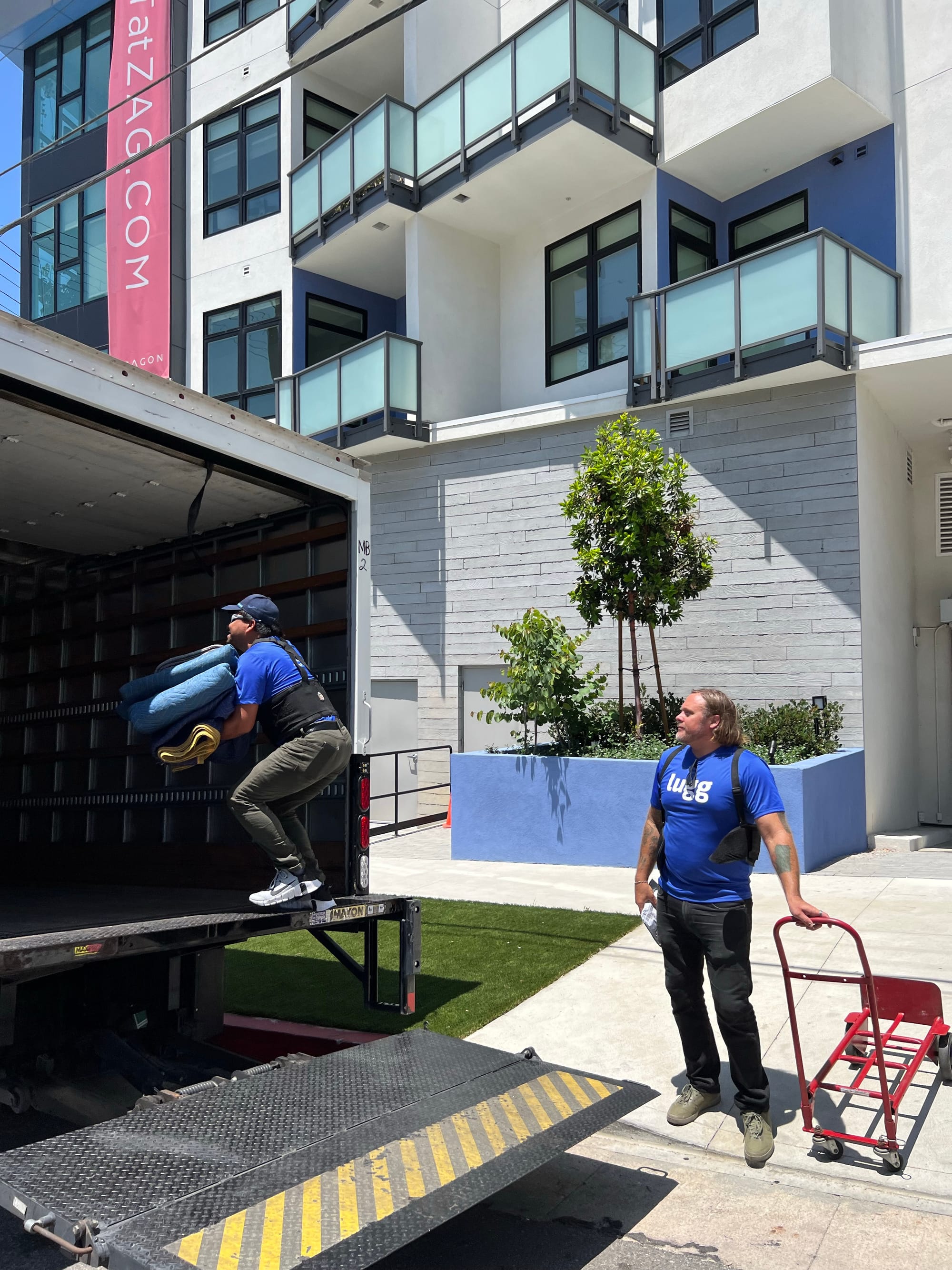Lugg mover carrying moving blankets into a box truck outside an apartment building, preparing for an apartment move.
