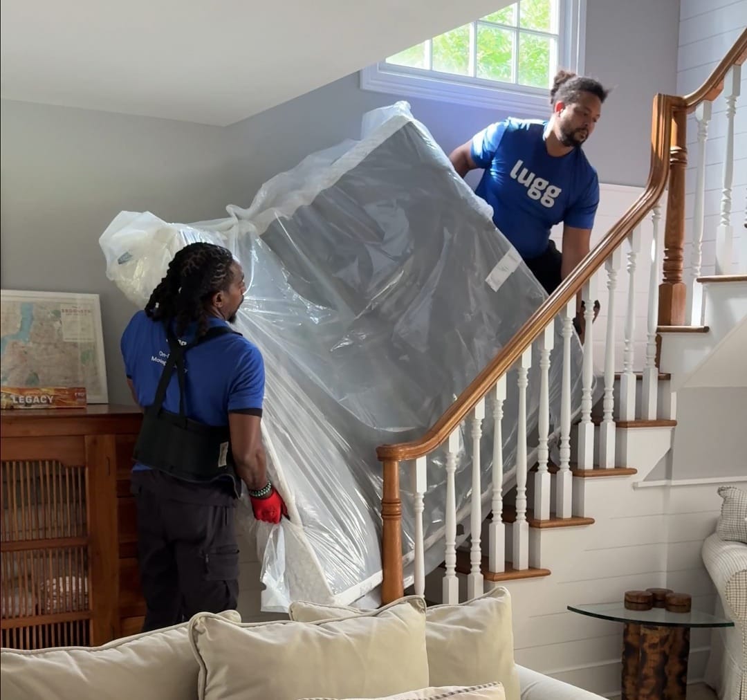Two Lugg movers carefully carrying a mattress down a narrow home staircase.