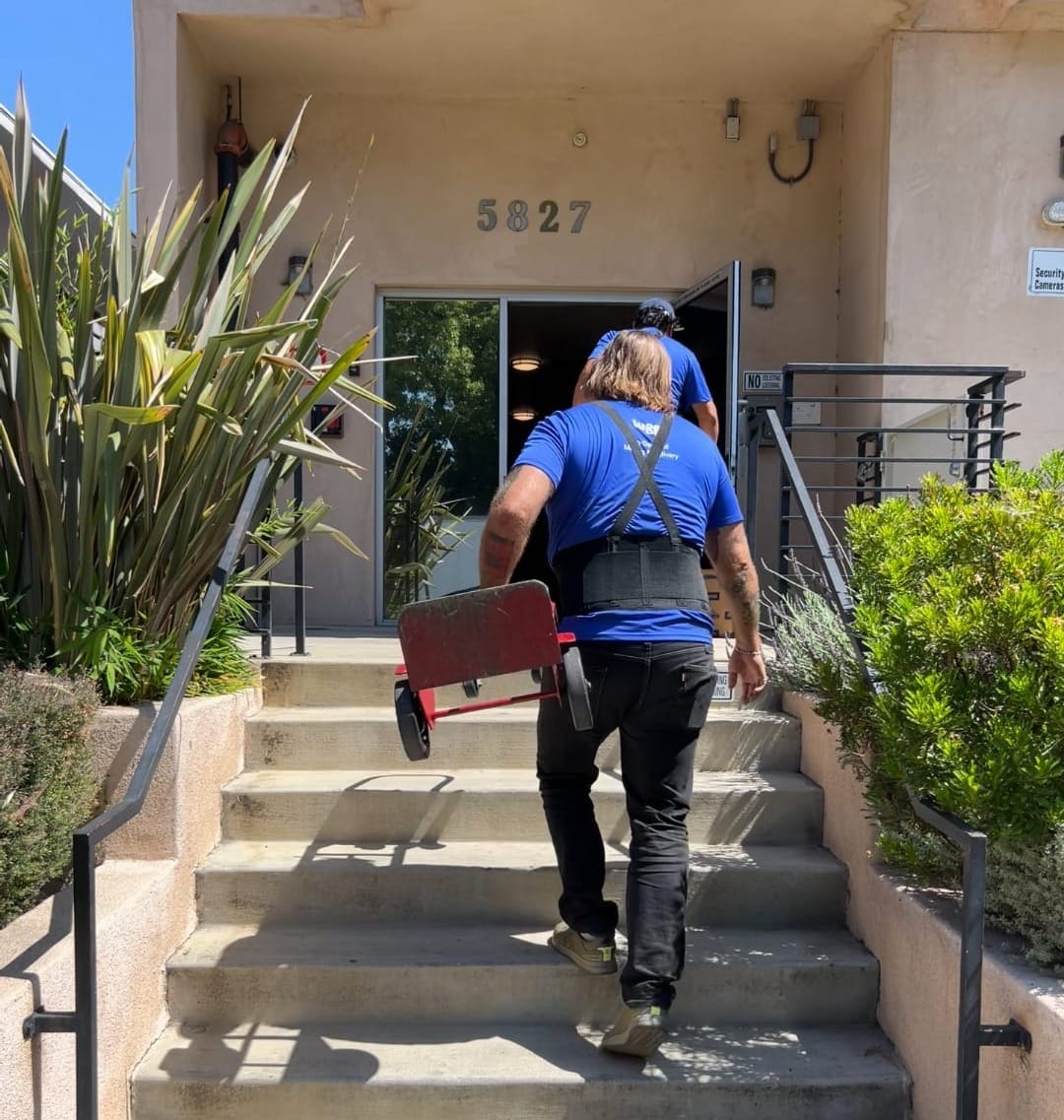 Two Lugg movers carrying a moving dolly and other equipment into an apartment building
